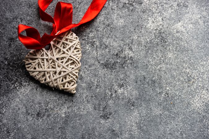 Thatched heart ornament with red ribbon on grey counter