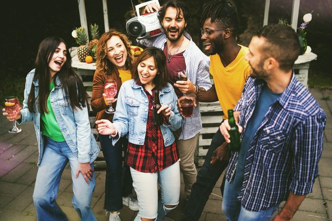 Happy friends dance at backyard party with boombox & drinks