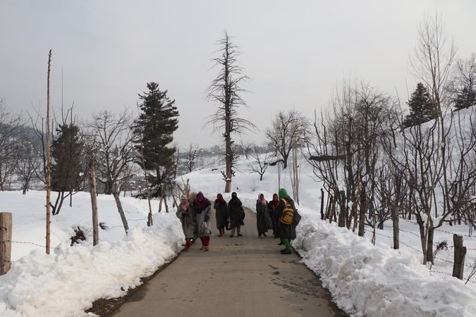 Back view of young women with backpacks walking on pathway between snow in Himalayan Kashmir, India
