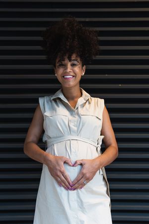Smiling Black woman showing heart gesture on pregnant tummy