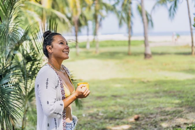 Relaxed woman enjoying hot drink and standing on exotic lawn
