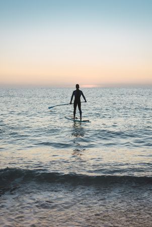 Man practicing paddle surfing with neoprene in a sunrise