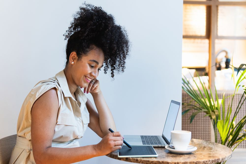 Smiling Black woman working on graphic tablet in cafe