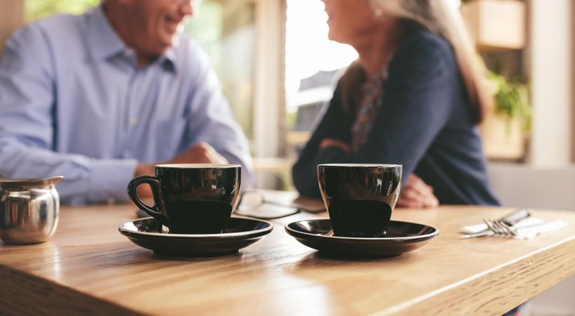 Two cups of coffee on table with couple sitting in background at a cafe