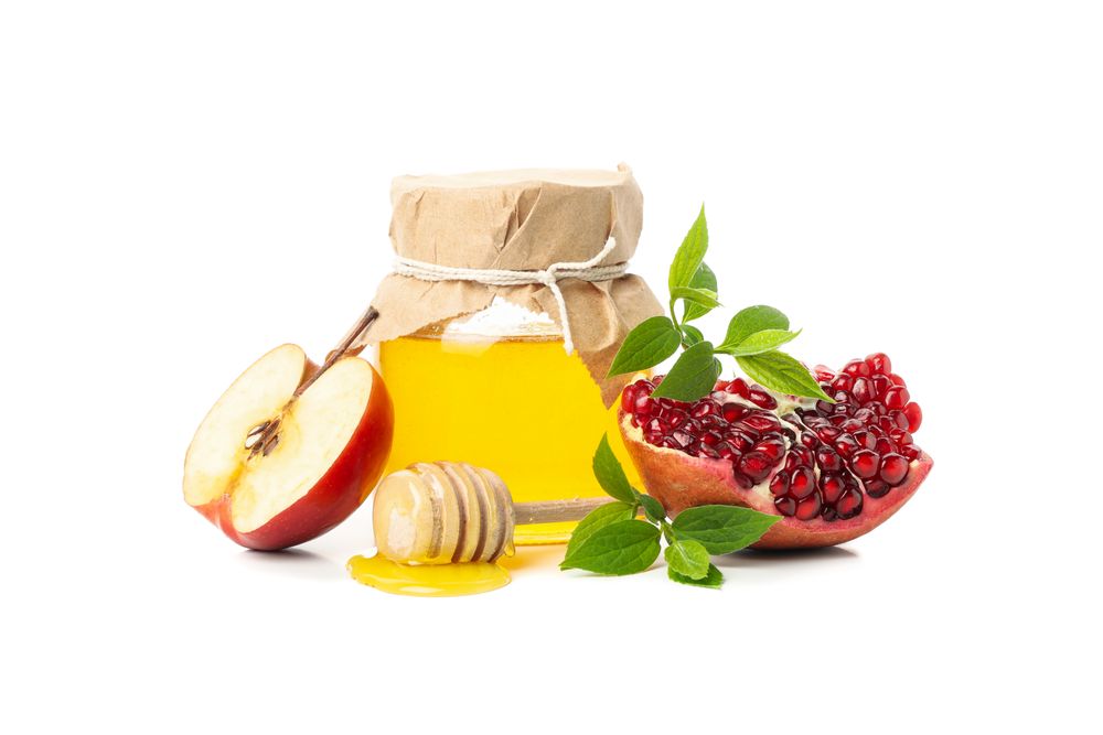 Pot of honey with dipper, split pomegranate and apples