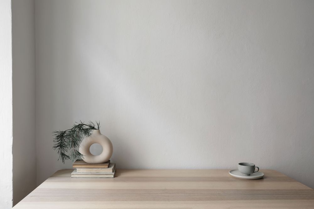 Modern vase on old books with pine tree branches and cup of coffee on beige table