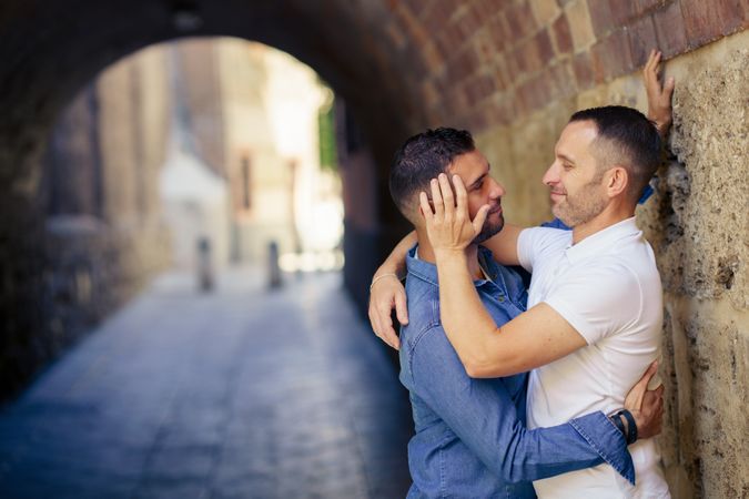 Two men facing each other and touching with one touching the others face  under a city bridge