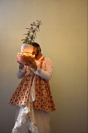Indian man in kathak dress holding Tulsi plant with diyas and dancing