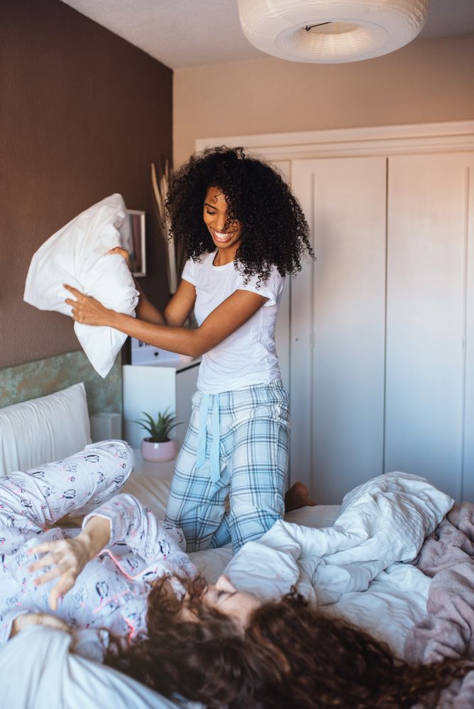 Young female friends fighting with pillows in the bed
