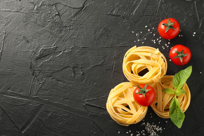 Pasta, tomatoes and salt on dark background, space for text