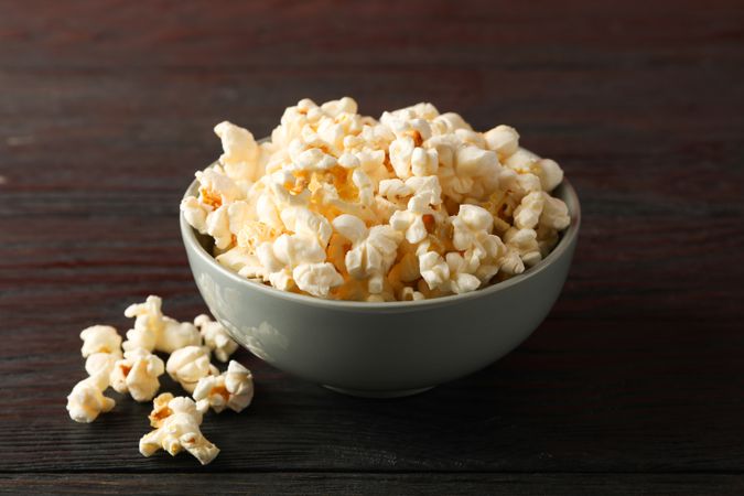 Bowl with popcorn on wooden background, space for text