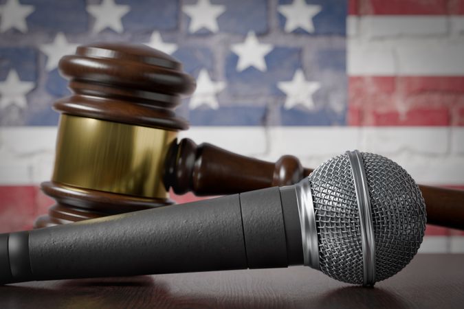 Microphone and Gavel Resting on a Table with the American Flag Painted On A Brick Wall Behind.