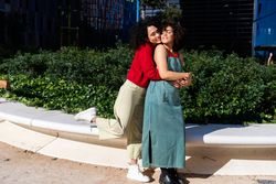 Fun female couple holding each other in city park with office buildings in background