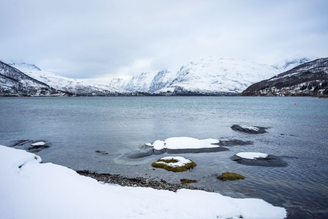 Tranquil lake against snowy hills in cold overcast weather