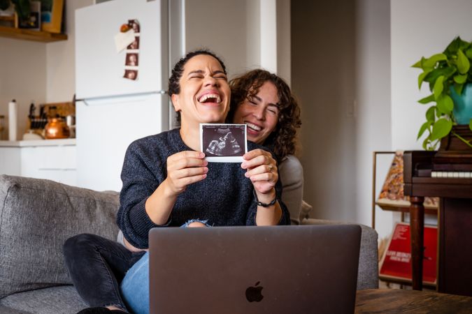 Two women happy sharing their  sonogram picture over video chat
