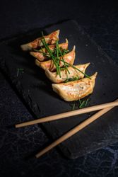 Fried Japanese dumplings with green onion on slate board