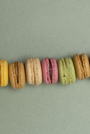 Line of pastel tasty macaroons over a green background, vertical