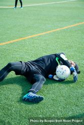 Injured football player laying on green grass with the ball 4AXOY5
