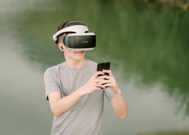 Young teenager with virtual reality glasses and smart phone outdoors