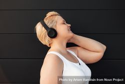 Side view of woman with eyes closed listening to headphones 0JyeZb