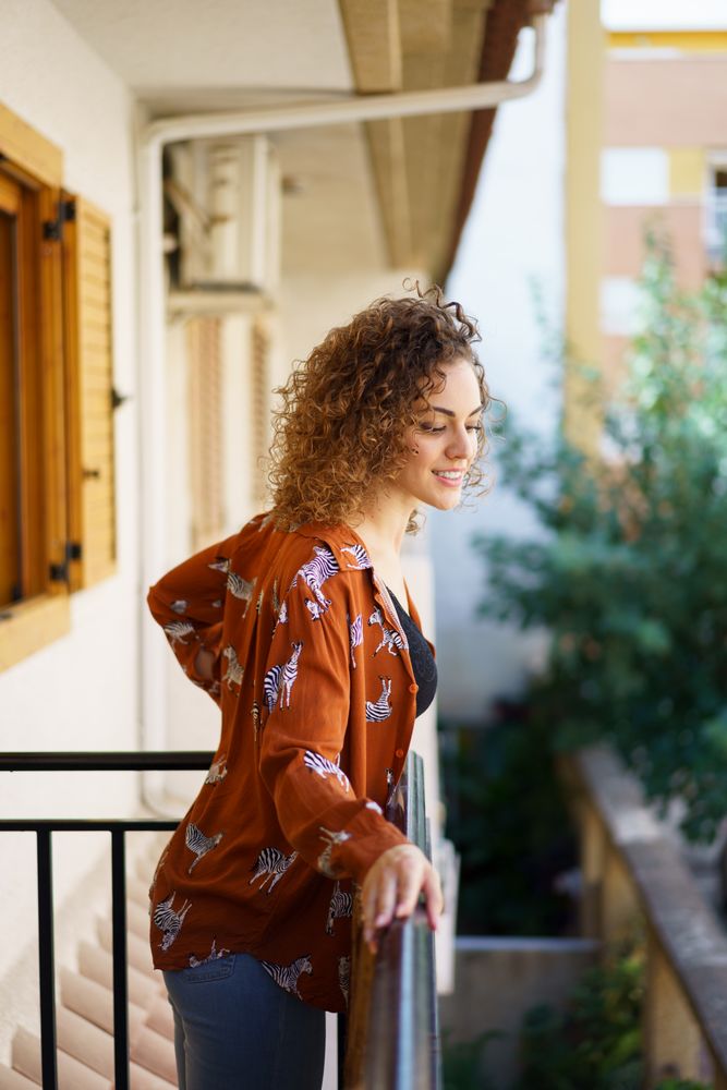 Smiling young woman standing on balcony in modern apartment