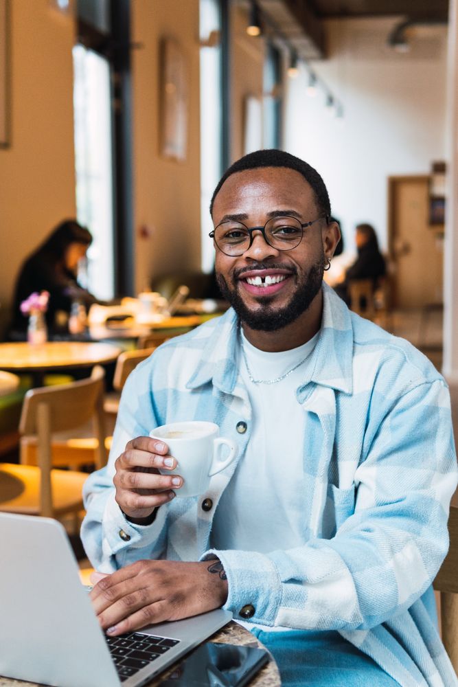 Delighted Black man with coffee browsing laptop