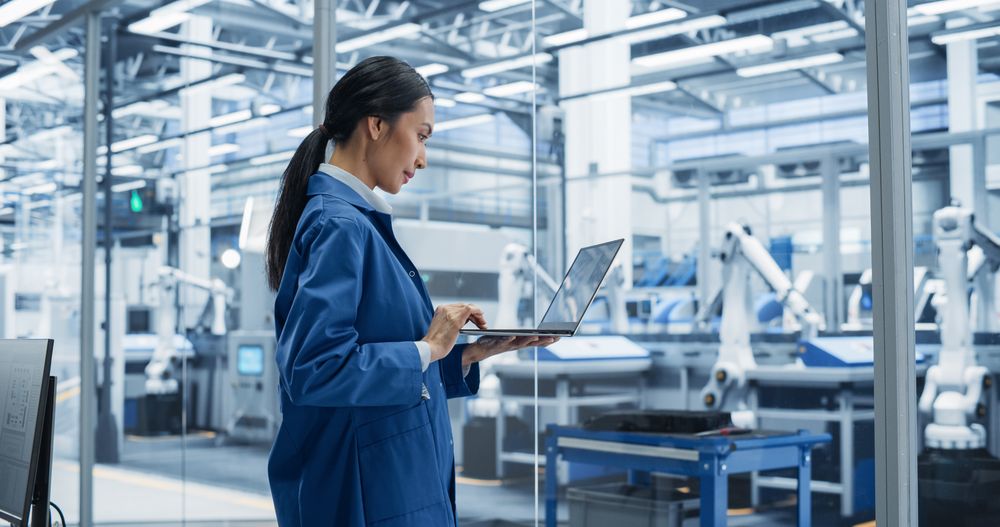 Southeast Asian Engineer Using Laptop Computer and Looking Around a Factory Facility with Equipment Producing Modern Electronic Components for Advanced Industrial Needs
