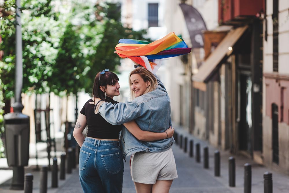 Lesbian couple with LGBT flag walking on street