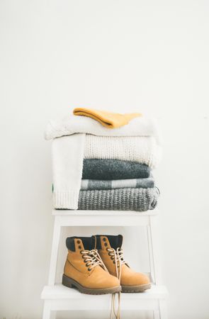 Pile of folded sweaters on light background with yellow boots, vertical composition, copy space