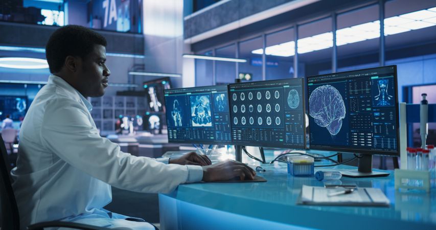 Black Male Neuroscientist Using Desktop Computer To Analyze MRI Scans Of Brain In Medical Research Center Laboratory.