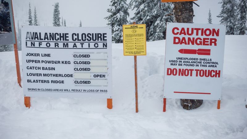 Sign with ski area boundary title on hill with snow and clouds between mountains