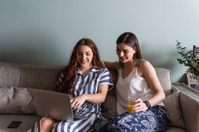 Smiling girlfriends sharing laptop on couch at home