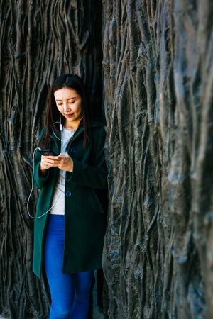 Asian female listening to music near rough wall