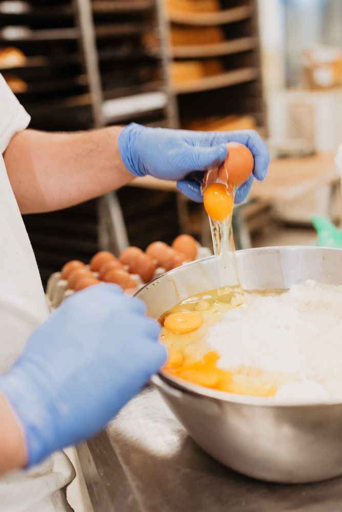 Crop baker breaking egg for pastry