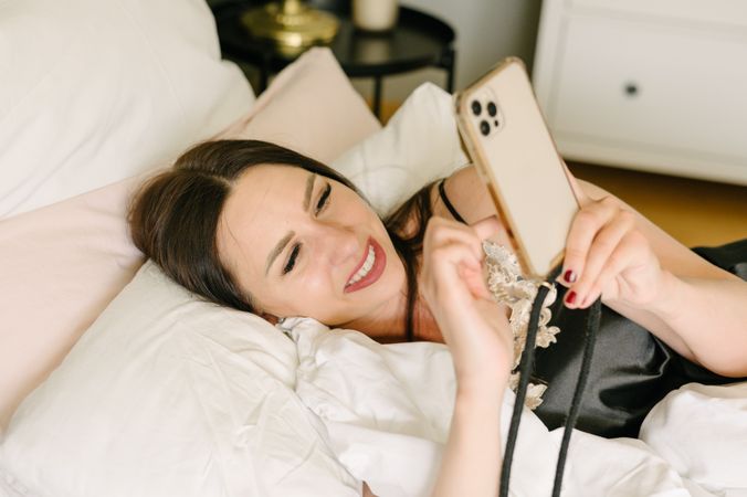 Young woman lying on bed and using smartphone