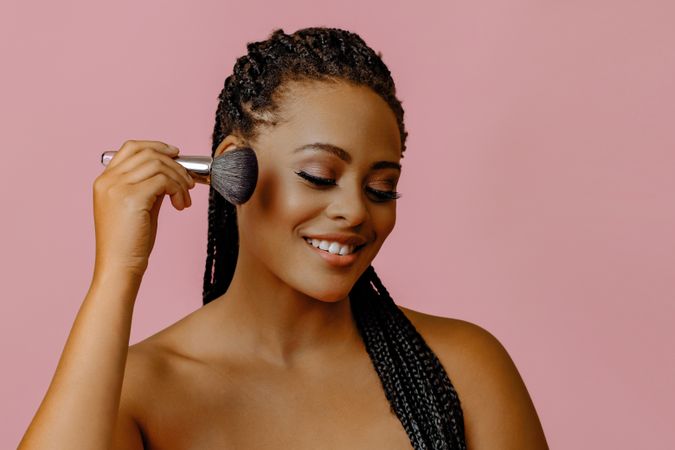 Smiling Black woman with make up brush to her cheek
