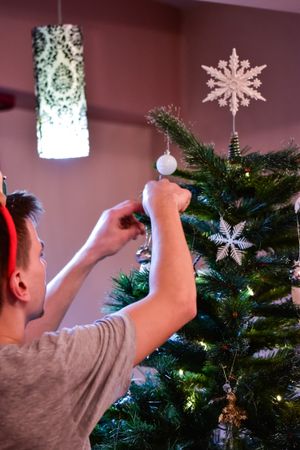 Back view of young man decorating Christmas tree with light ornament