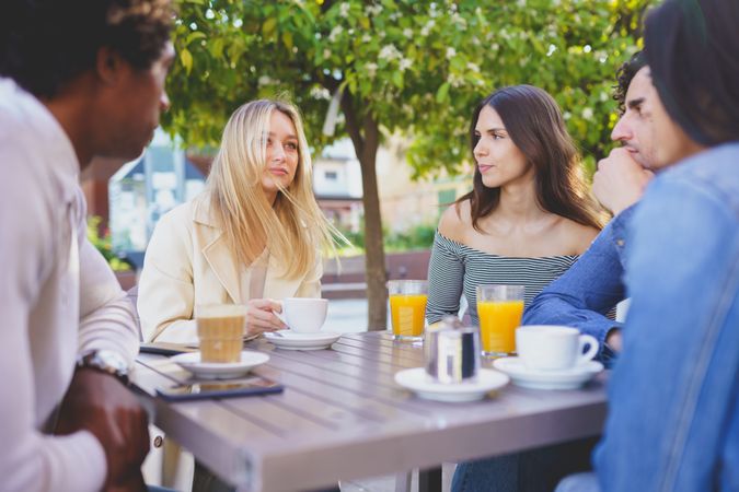 Diverse group of friends having a conversation over coffee and juice at outside table