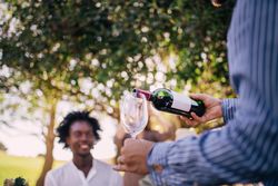 Man beginning to pour a glass of red wine outdoors