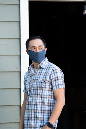 Portrait of man standing outside in front of garage in PPS mask smiling and looking to the side