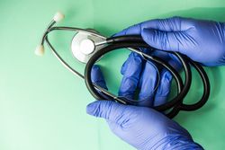 Looking down at green table with hands in blue latex gloves holding stethoscope