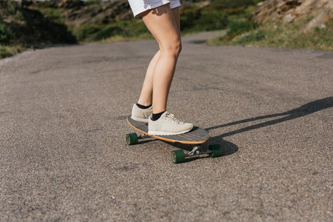 Anonymous woman riding longboard on asphalt road