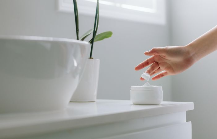 Close up of female hands taking moisturizing cream from bottle in bathroom