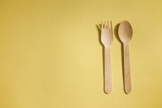 Disposable fork & spoon on yellow background with copy space