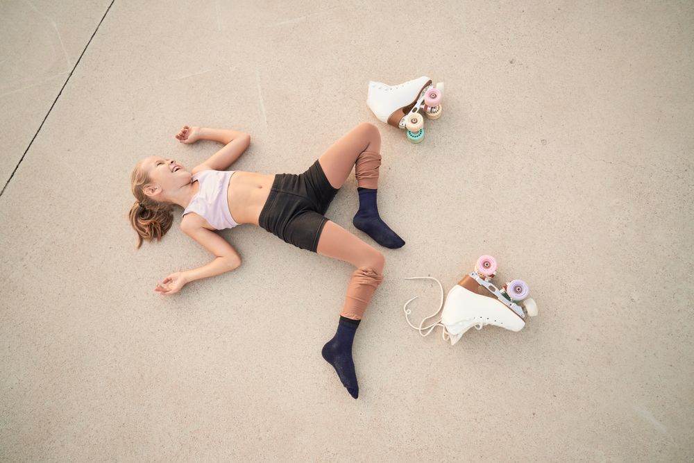 Laughing girl lying on concrete ground near quad roller skates