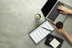 Top view of a person at a grey desk with calendar, laptop, cactus and coffee