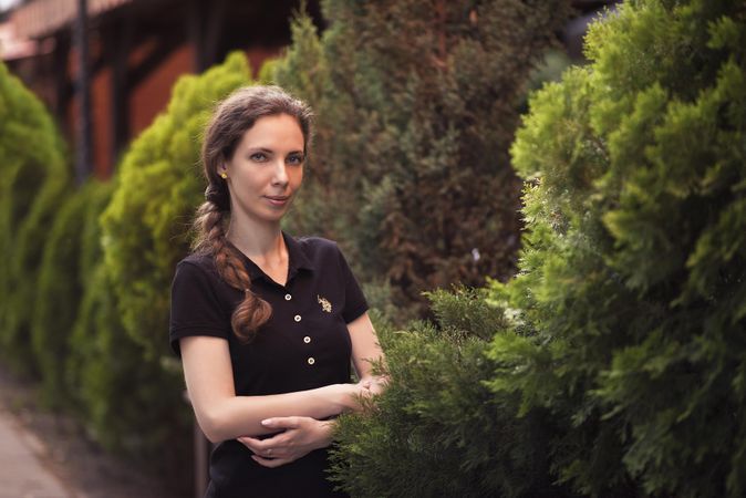 Woman in dark top crossing her arms standing beside trees