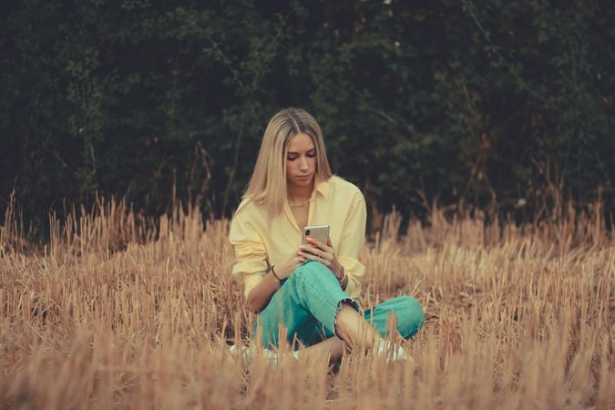 Woman using cellphone sitting on brown grass
