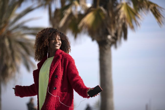 Smiling female in bright colors listening to music outside on street with palm trees