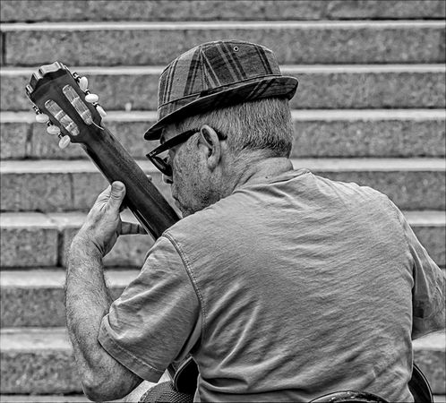 Back view of an older man with a hat playing the guitar